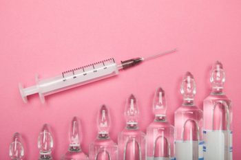 Increasing Dependence On Injections Of Hyaluronic Acid, Botox And Collagen. Syringe And Ampoules On A Pink Background.