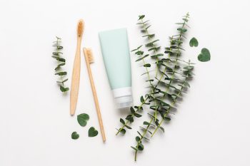 Bamboo Toothbrushes And Tube Of Toothpaste On White Background. Eucalyptus Branches. Natural Dental Care Concept
