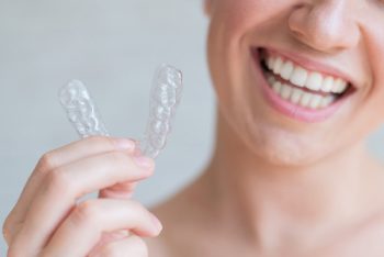 Close Up Of Orthodontic Silicone Transparent Teeth Aligner In Female Hands. A Woman With A Perfect Charm Smile Holds A Removable Night Retainer. Bracket For Teeth Whitening. Cropped Photo.